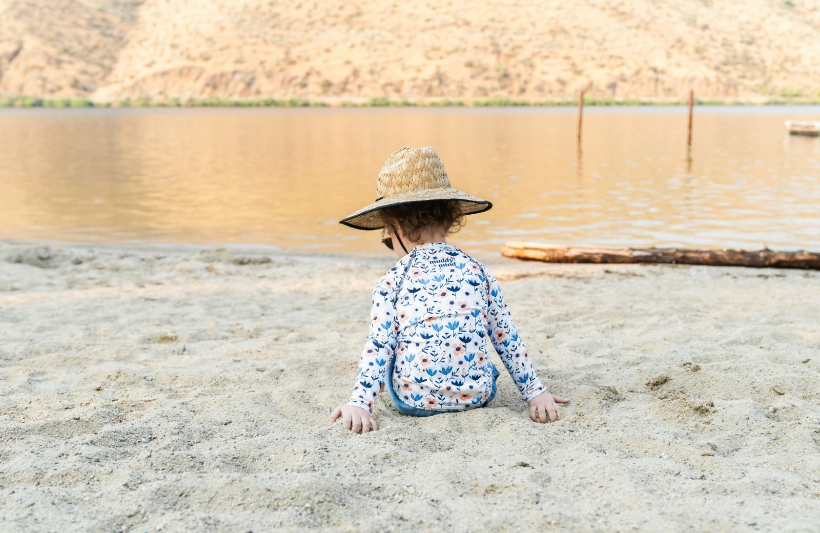 Niña con sombrero y camiseta de manga larga jugando en la arena